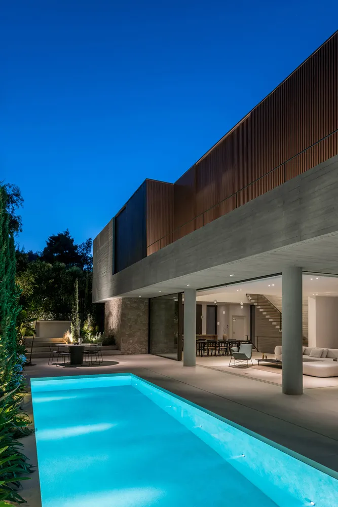 A modern house featuring a concrete, glass, and wooden exterior with a swimming pool and outdoor seating area.