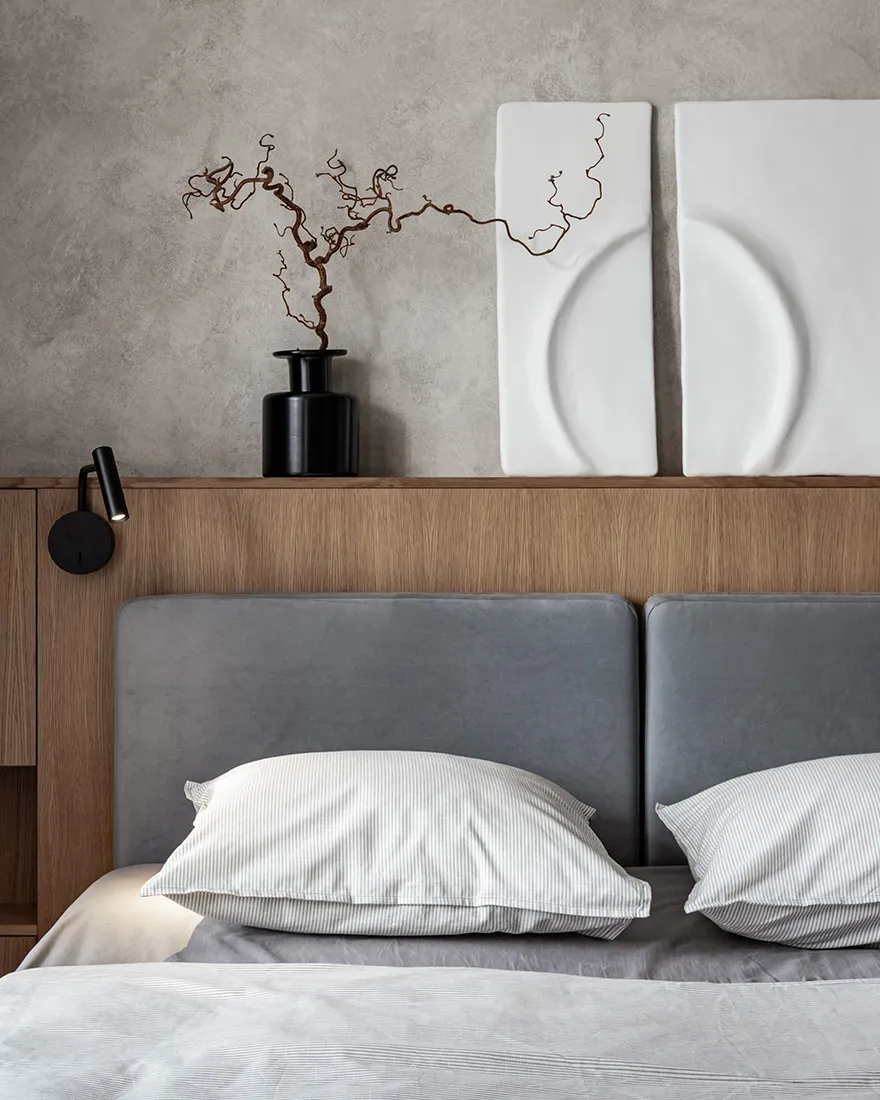 A minimalist bedroom featuring a concrete texture wall with a modern wooden headboard and simple bedding.