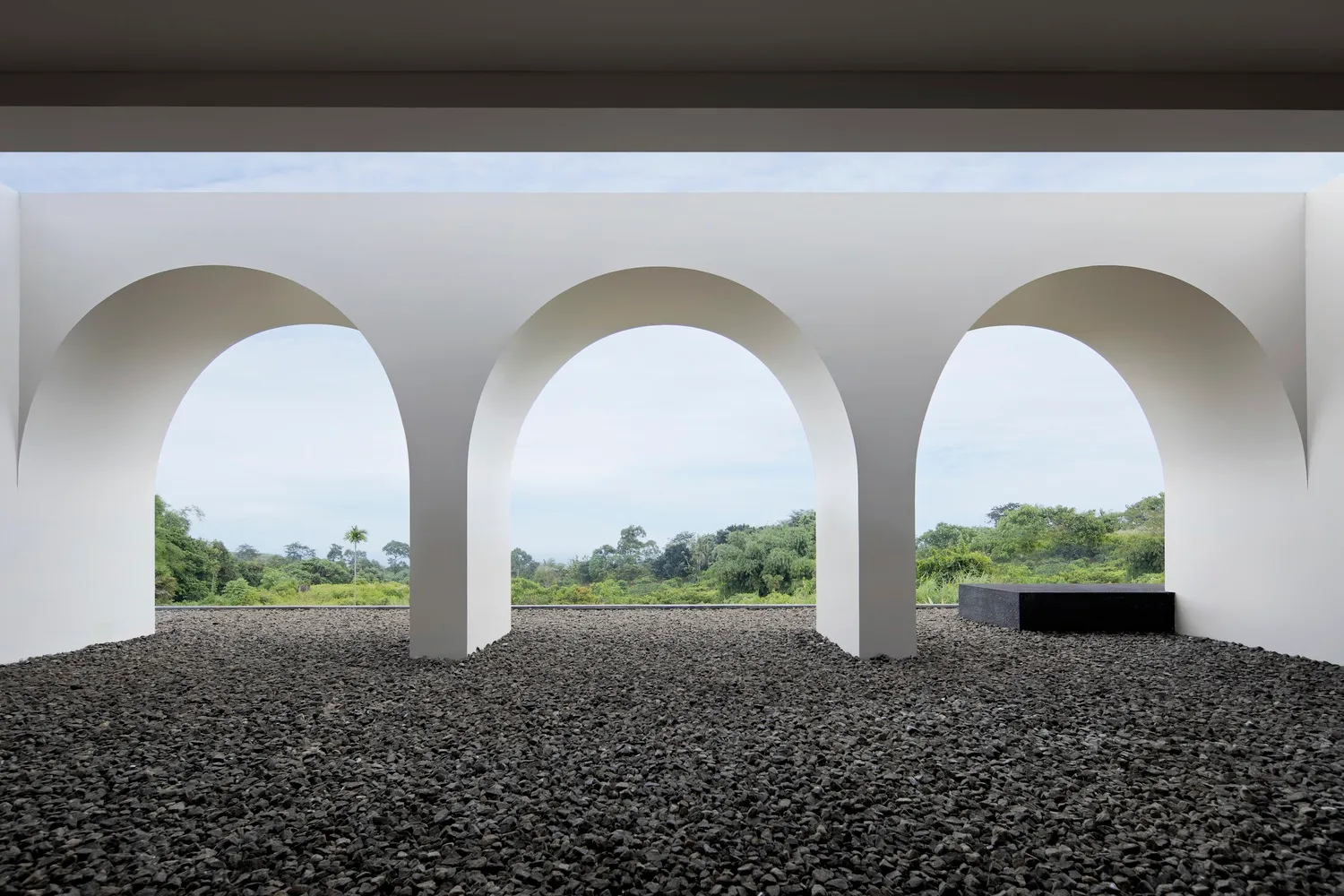 A view through an arched corridor of a modern interior with a concrete floor and natural landscape outside.