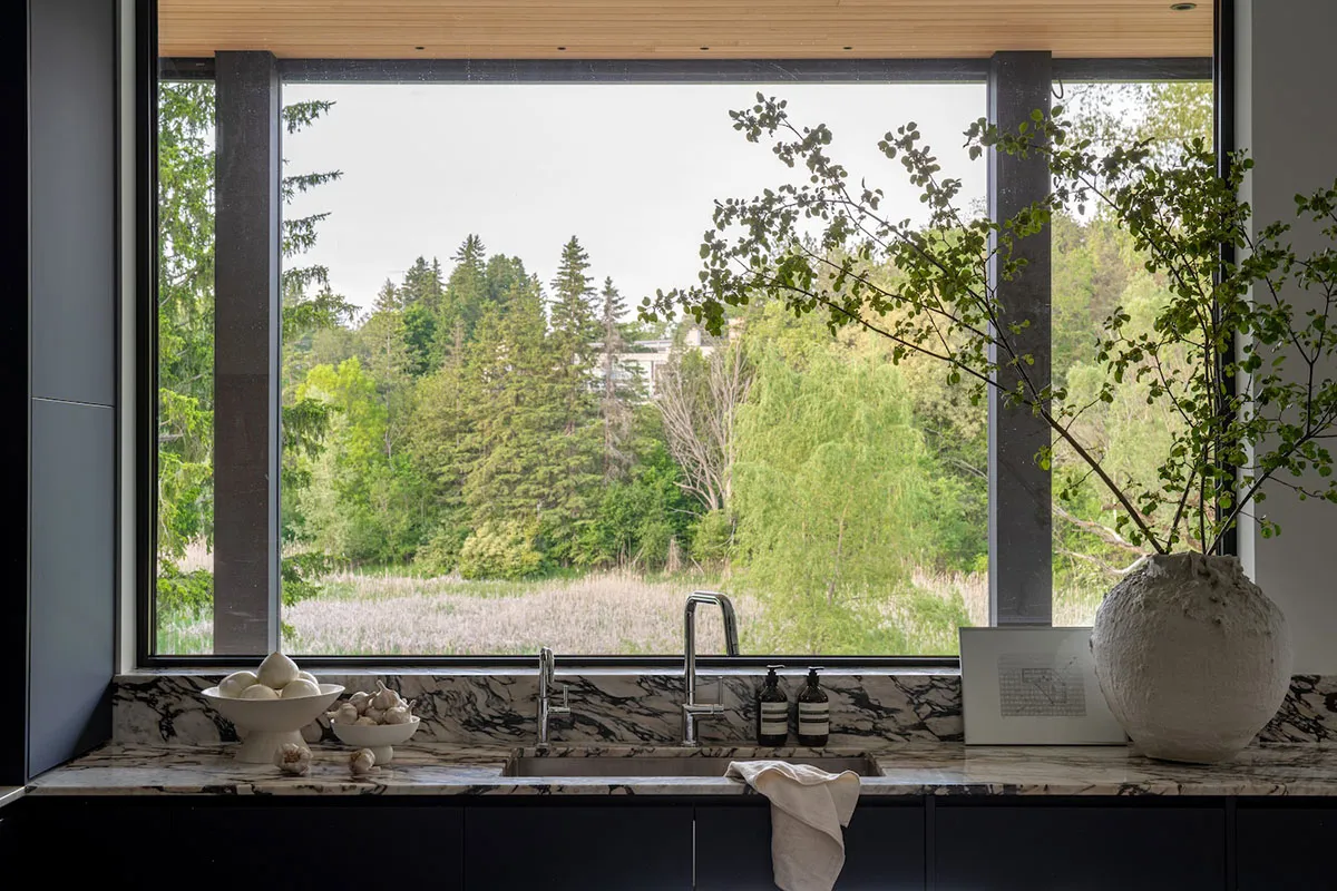 A modern kitchen with a marble countertop and sink overlooking a forested landscape.