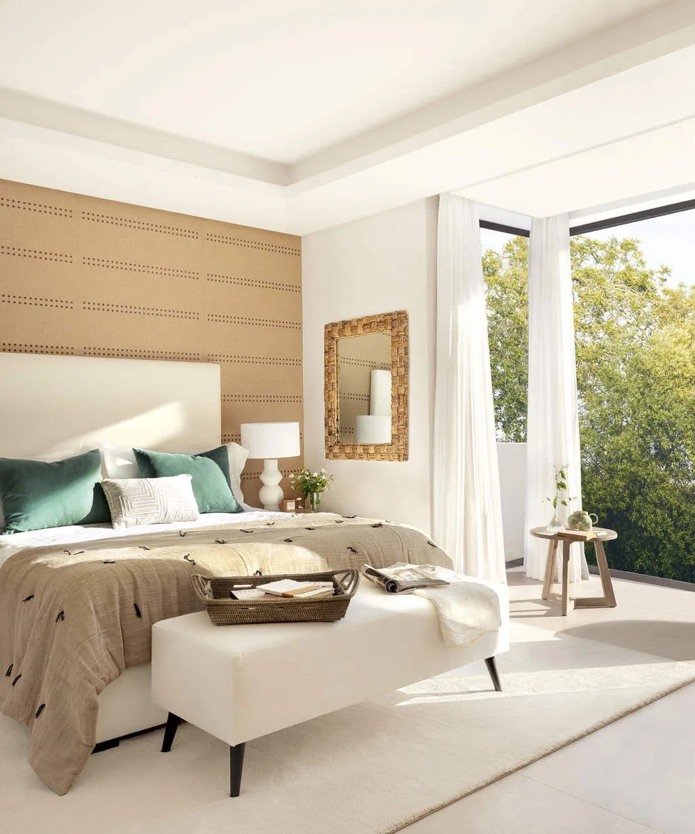 A minimalist bedroom featuring a bed with green and white pillows, a woven headboard, and a large window with sheer curtains,
