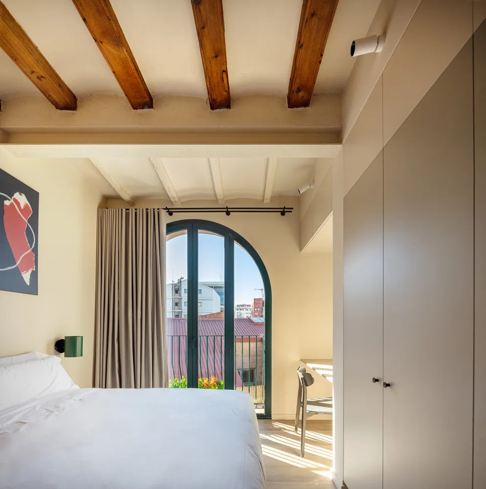 Modern minimalist bedroom with wooden beams on the ceiling, fabric curtains, and a white bed.