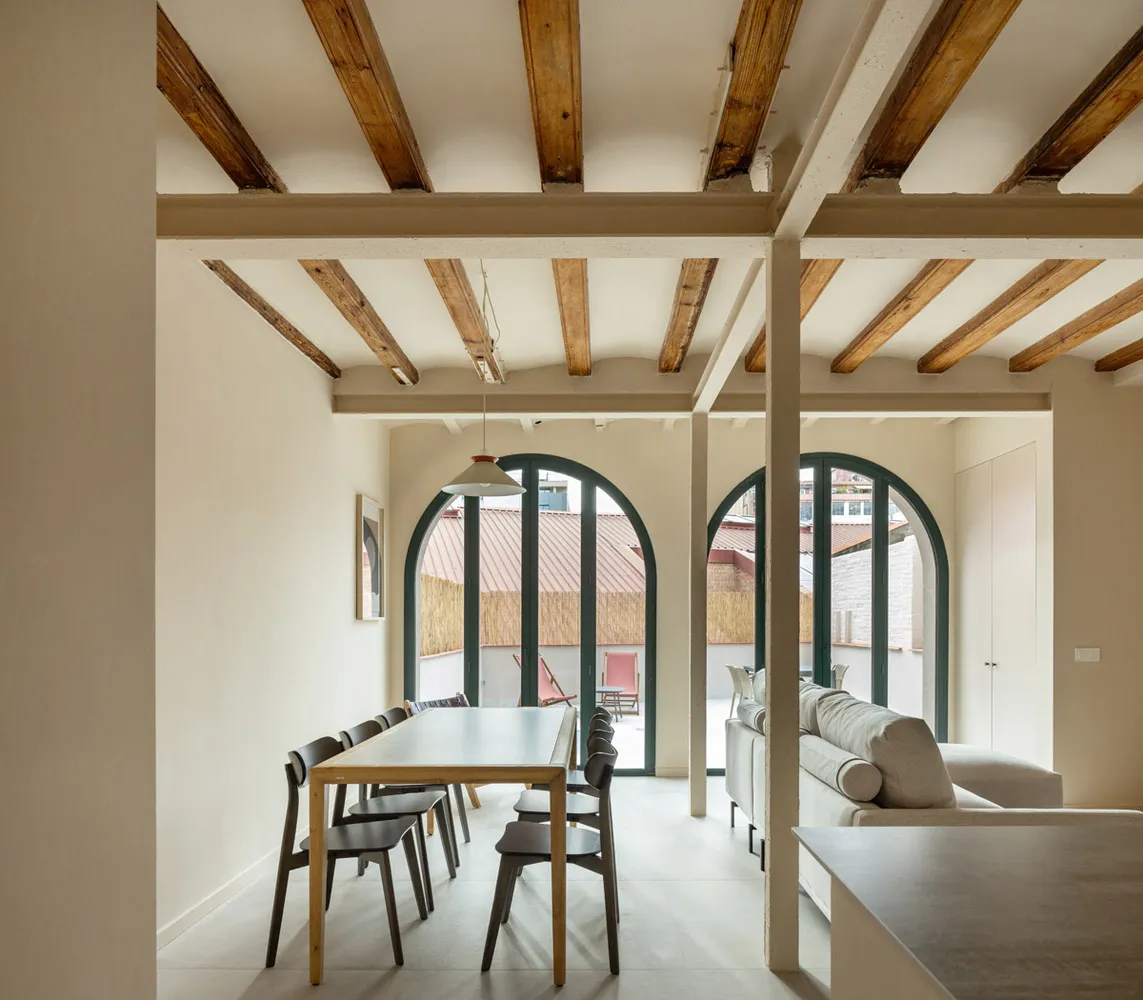 A modern interior space featuring white walls, wooden beams, and a comfortable seating area.