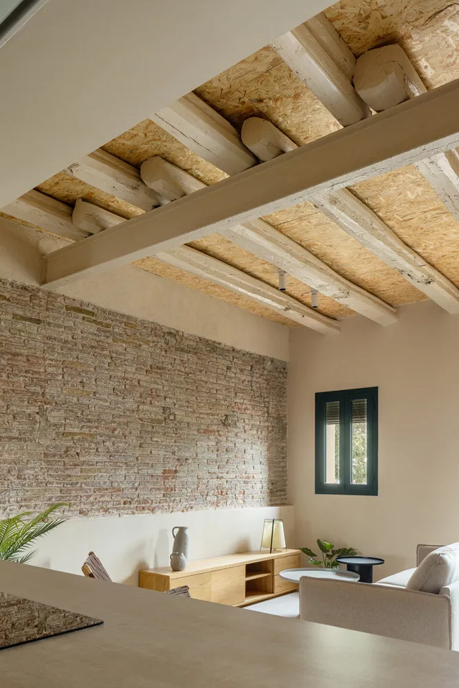 A modern living room with exposed brick walls and wooden beams on the ceiling.