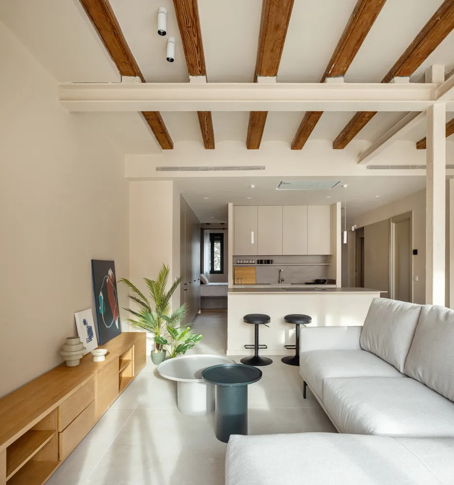 A modern living room with a white sofa, wooden flooring, and exposed wooden beams on the ceiling.
