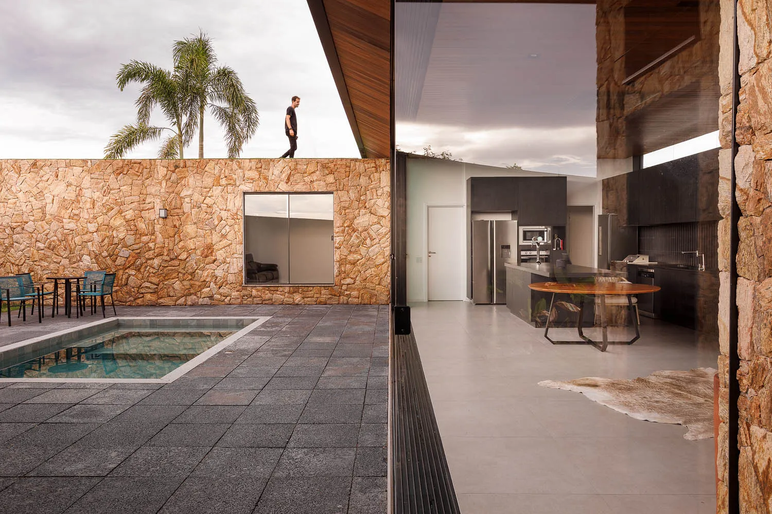 A modern residential interior featuring a concrete patio with a pool and seating area, a well-lit living space with a large k
