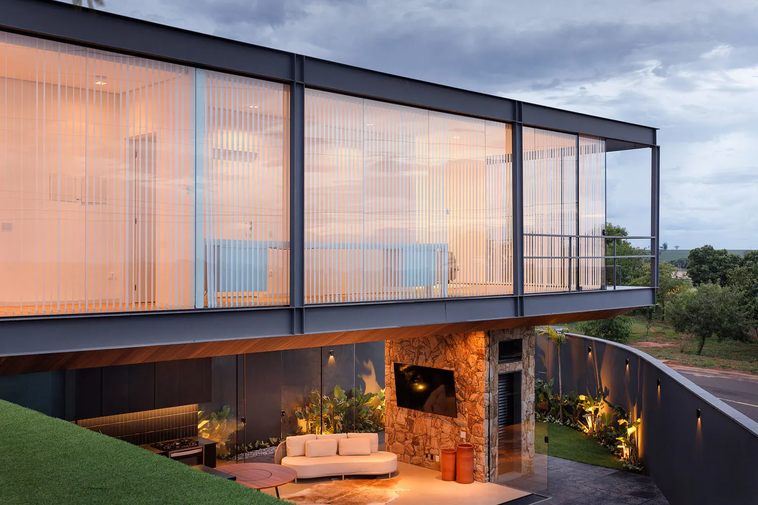 A modern house with a glass exterior featuring vertical blinds and a stone patio.