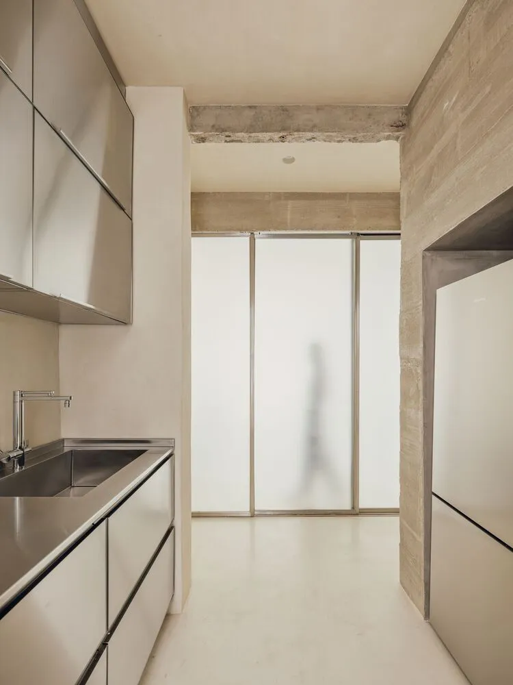Modern kitchen with metallic cabinets and sink, frosted glass partition, and white flooring.