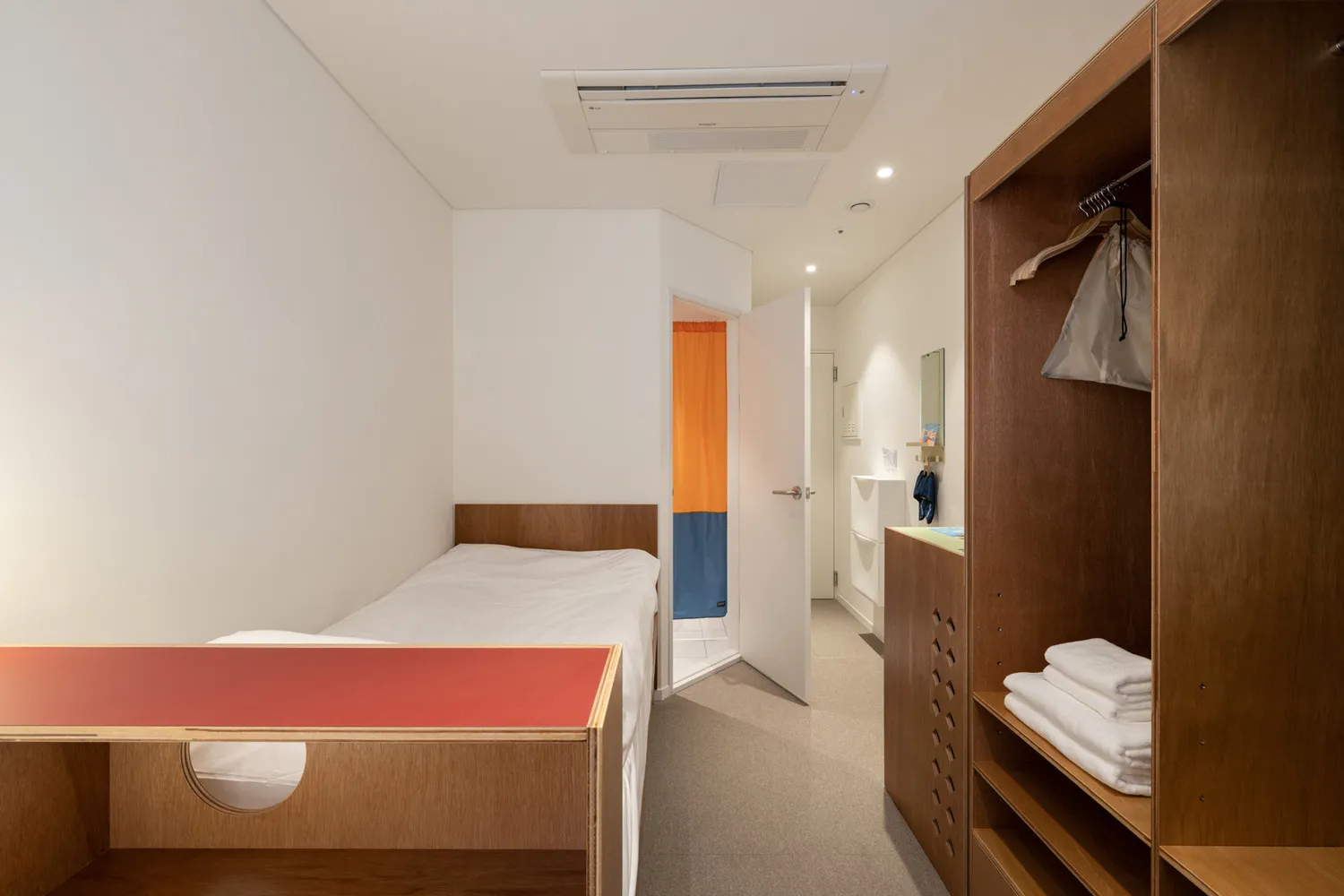 A minimalist bedroom with a bed, wooden furniture, and a red table.