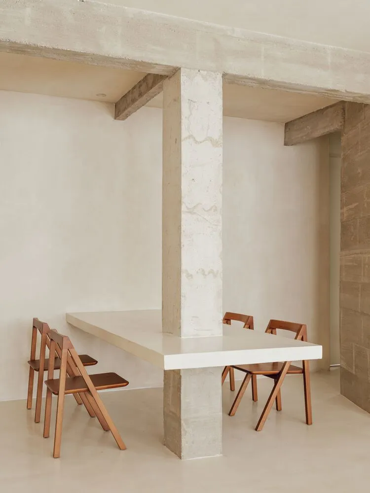 Modern minimalist dining room with concrete table and wooden folding chairs.