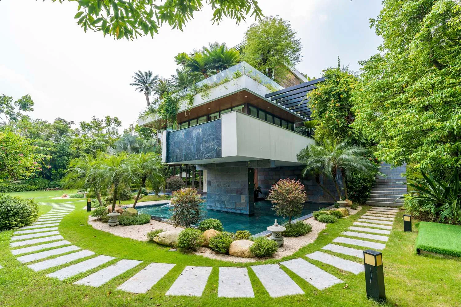 A contemporary residential house with glass walls and stone accents surrounded by lush greenery.