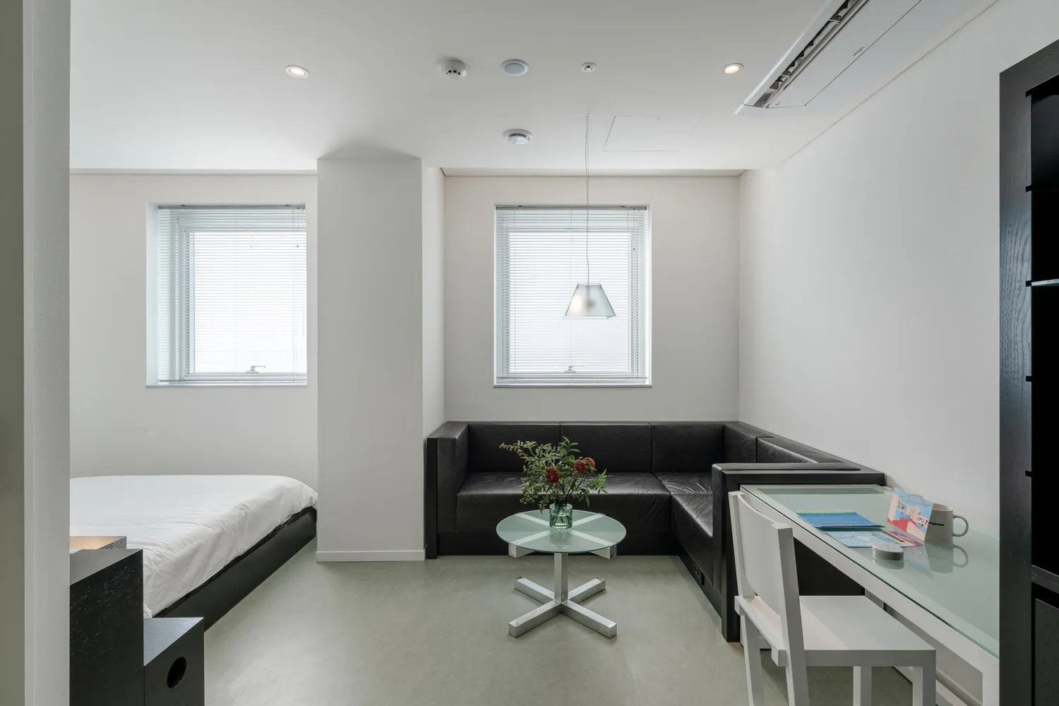 A minimalistic modern studio apartment with metallic accents and a fabric sofa, featuring a glass table and white walls.