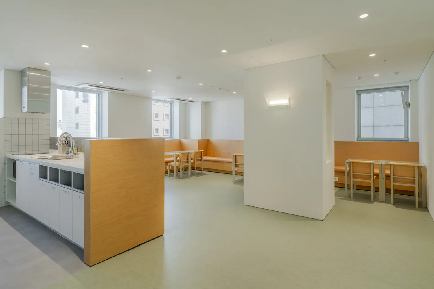 Bright, spacious community center interior with wooden benches and tables, concrete flooring, and large windows.