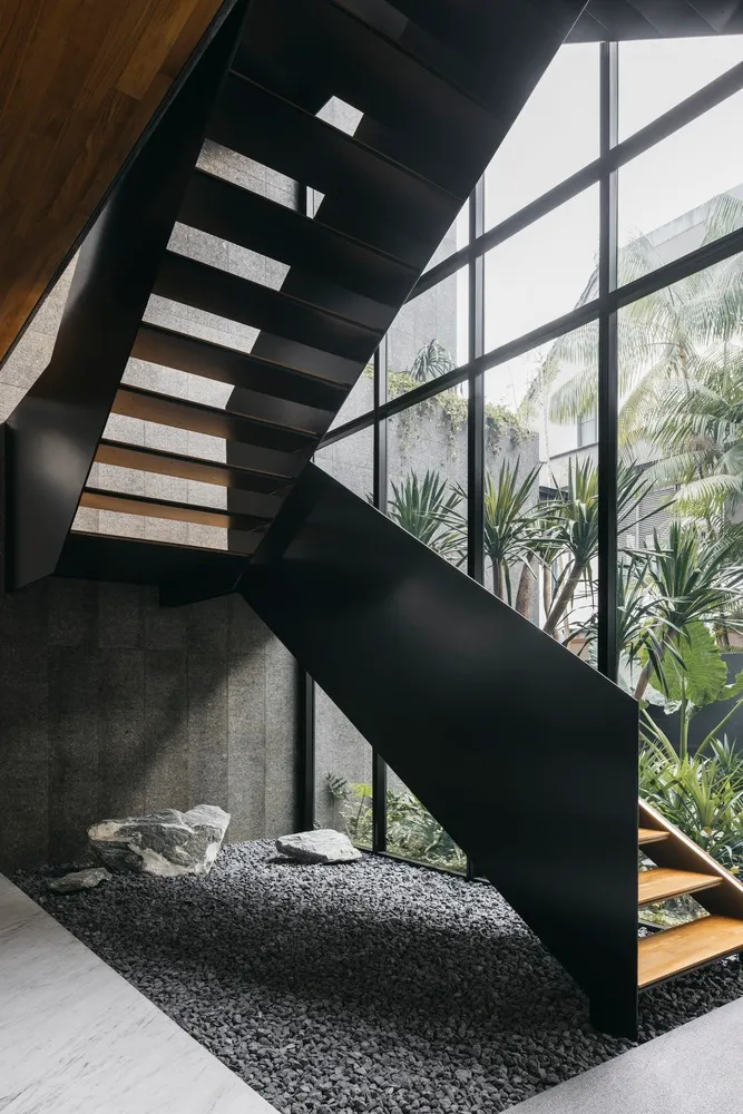 Modern industrial steel staircase with concrete floor, surrounded by large glass windows and greenery.