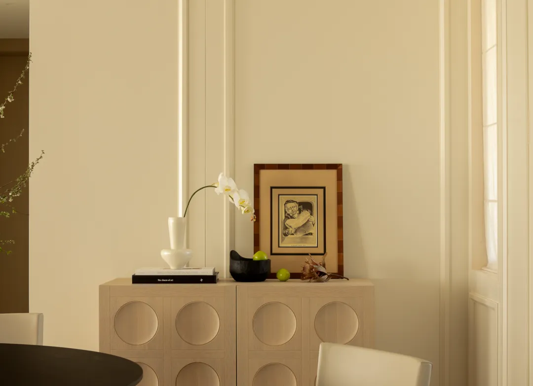 A minimalist interior design featuring a wooden cabinet with circular cutouts, placed beneath a window with natural light str