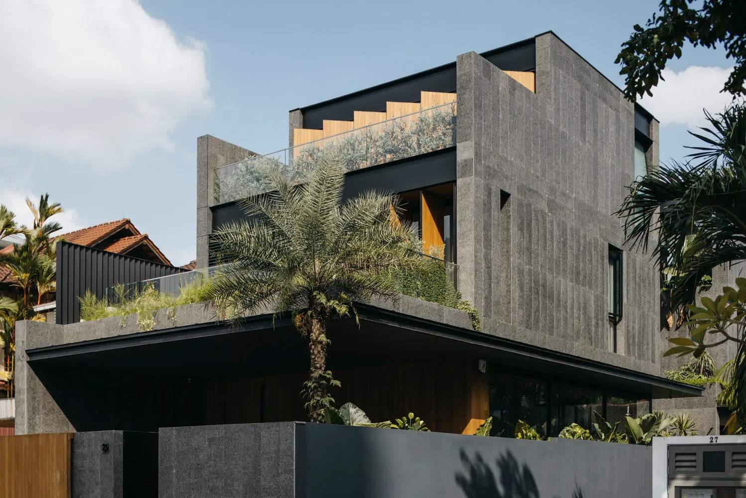 A modern residential building with a concrete exterior and tropical landscaping.
