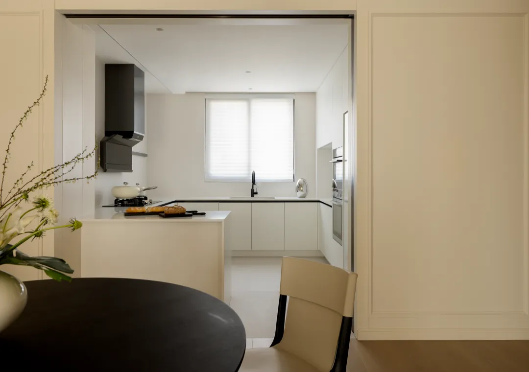 A modern kitchen with white cabinets, a black table, and a vase of flowers on the table.