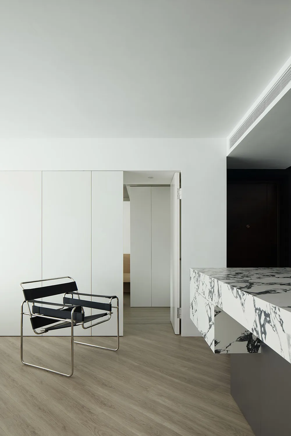 Minimalist living room with a marble countertop, white cabinets, a black chair, and a wood floor.