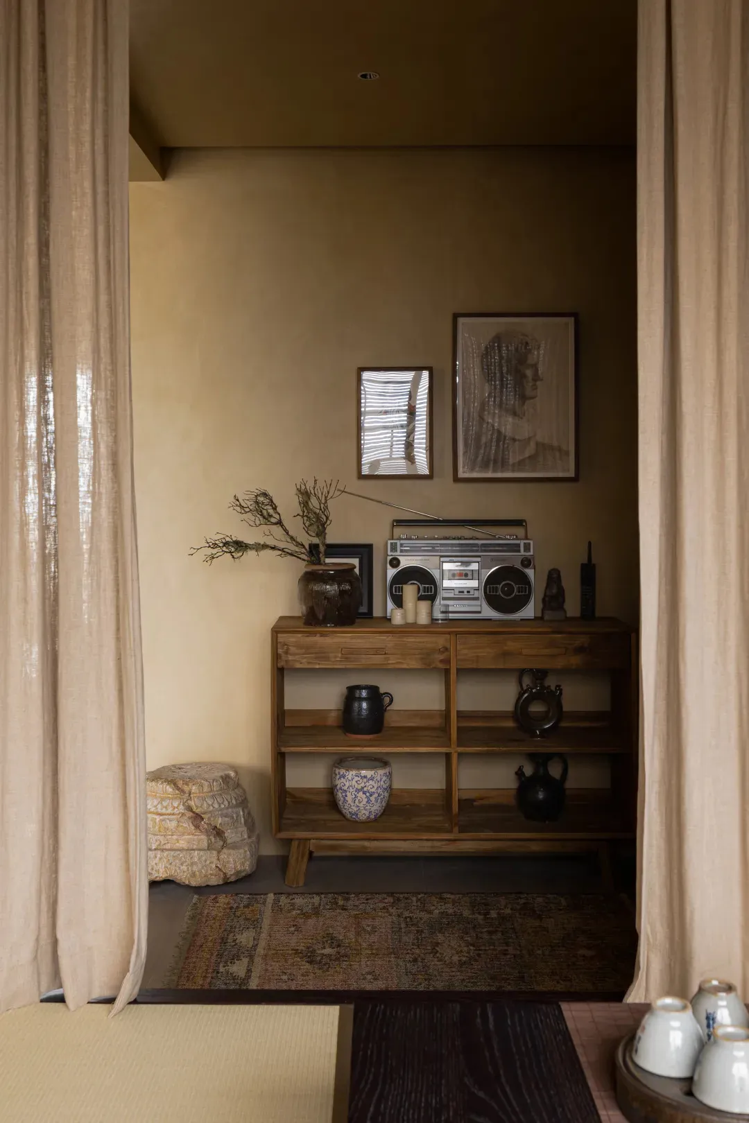 An industrial-style living room with a minimalist aesthetic, featuring a wooden cabinet, glass vases, and concrete flooring.