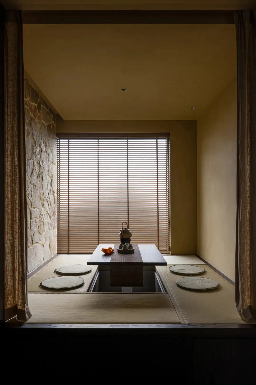 A minimalist tea room with bamboo flooring, wood walls, stone accents, and traditional seating.