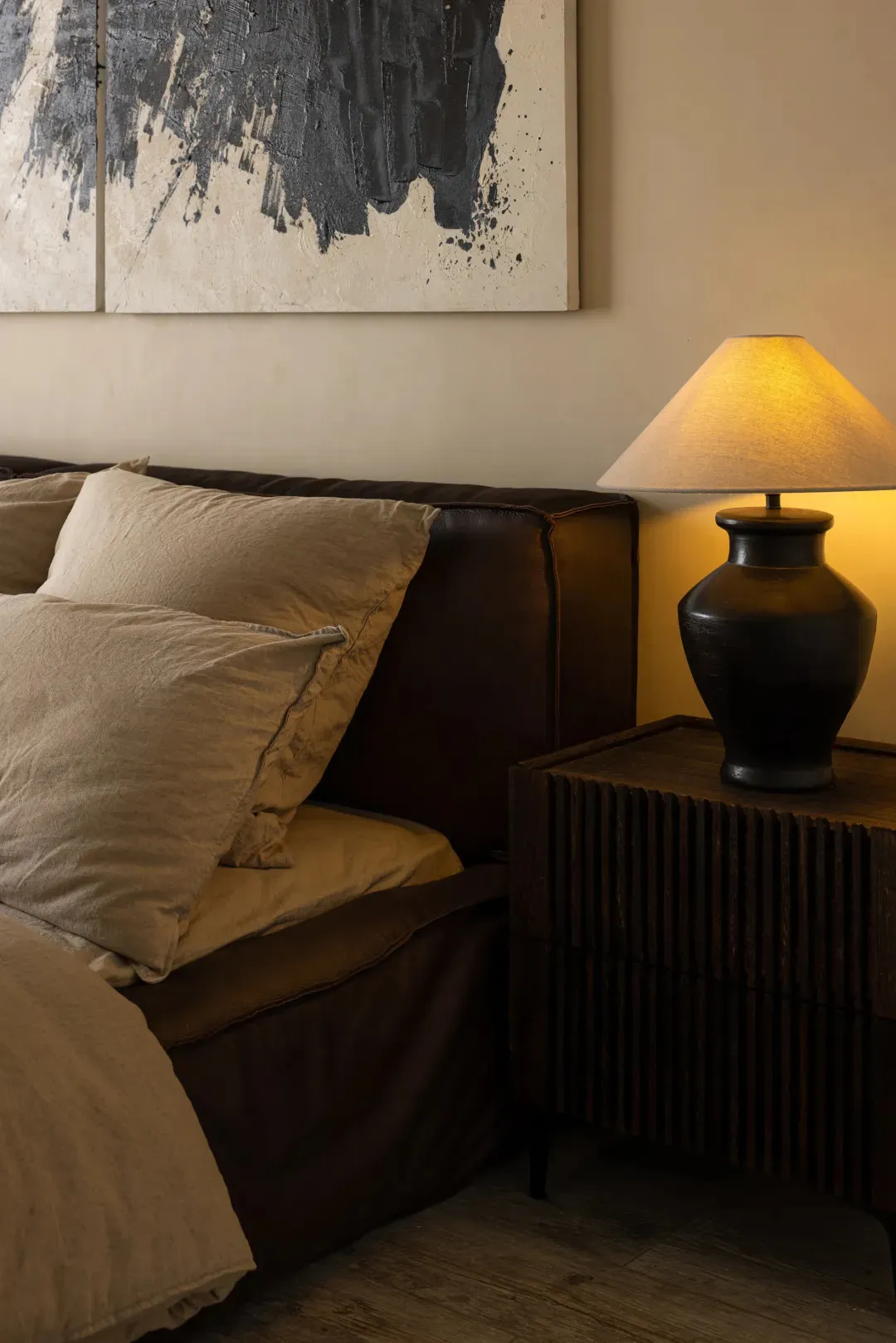 A modern bedroom featuring brown leather furniture and a lamp emitting warm light.