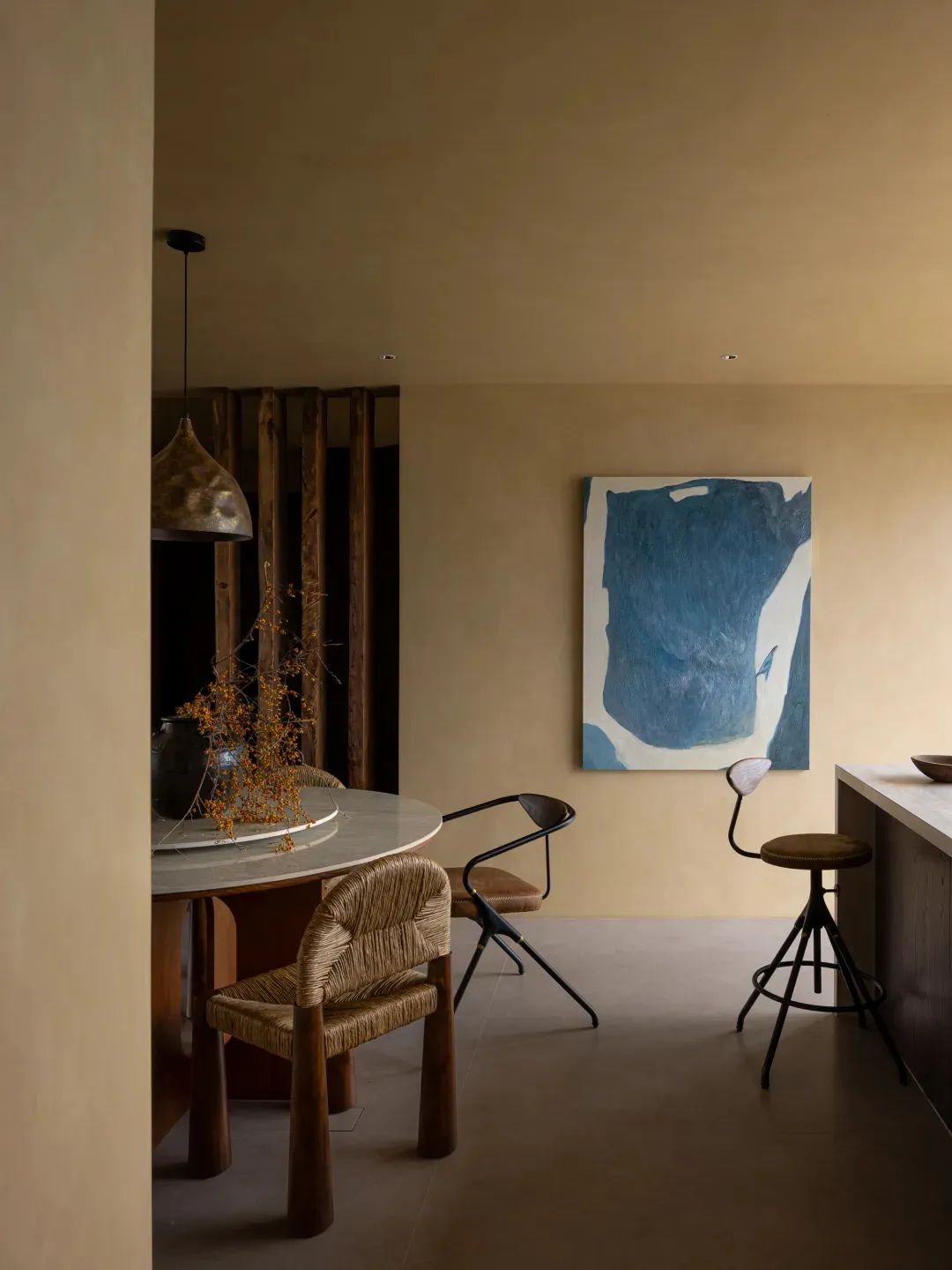 A modern dining room featuring a round marble table surrounded by wooden and woven chairs, a blue abstract painting, and a me