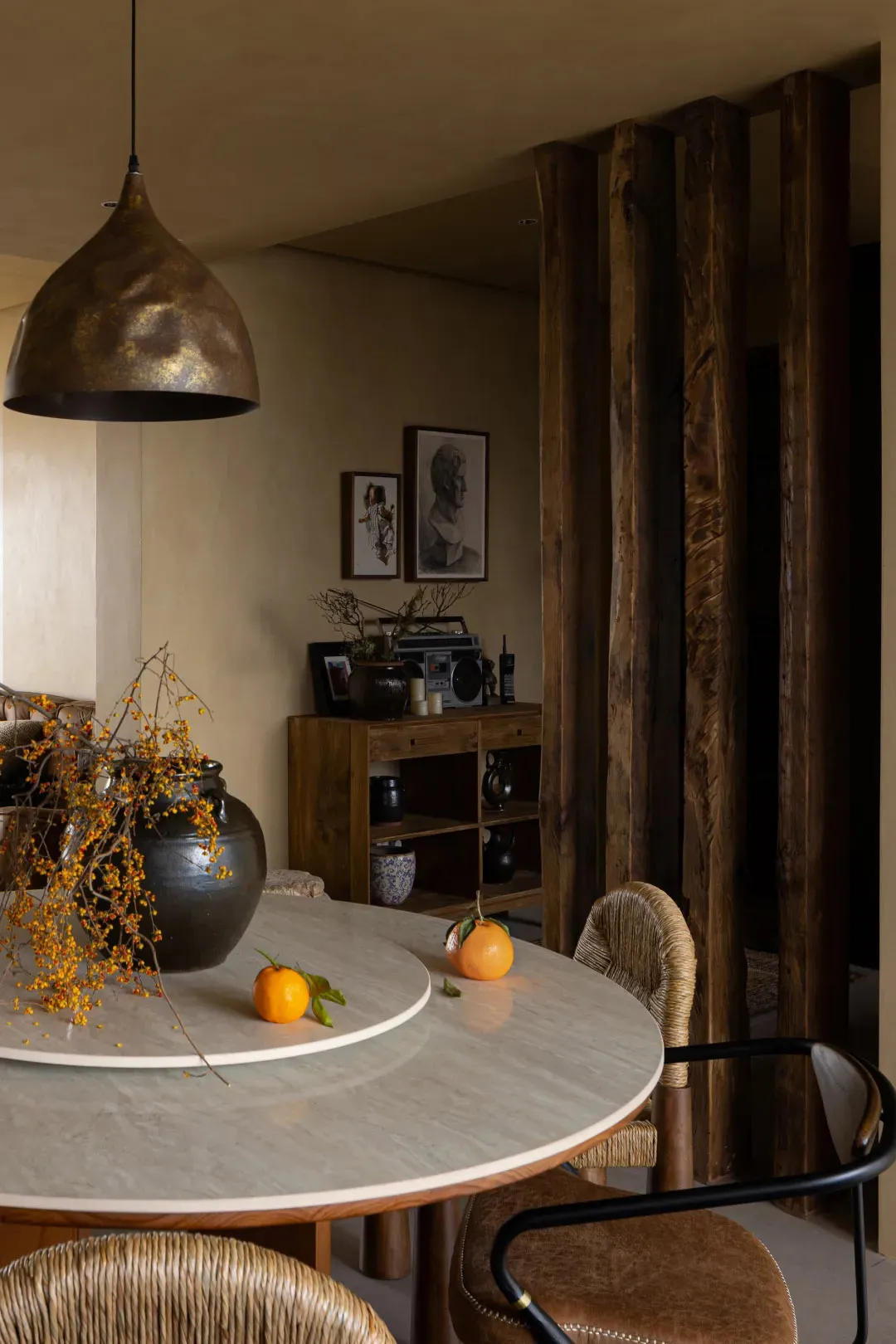 A modern dining room featuring a round marble table with a metal pendant lamp and wooden details.