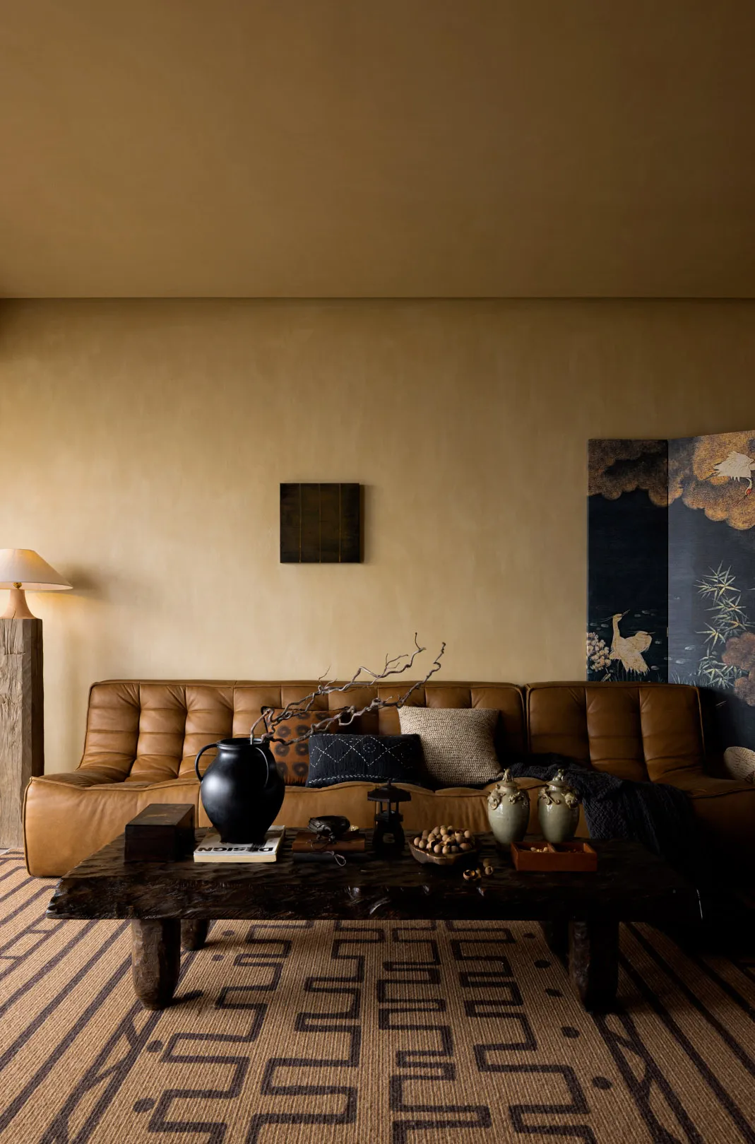 A modern living room featuring a brown leather sofa, a wooden table with decorative items, and a floor lamp in the corner.