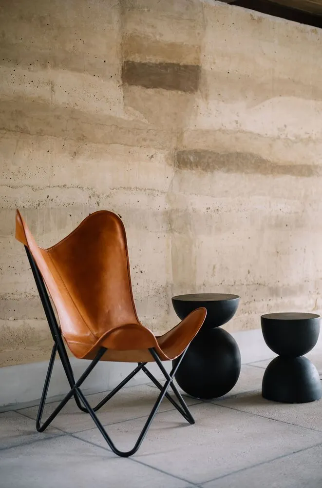 A modern butterfly chair with a black frame and leather upholstery paired with two black side tables.