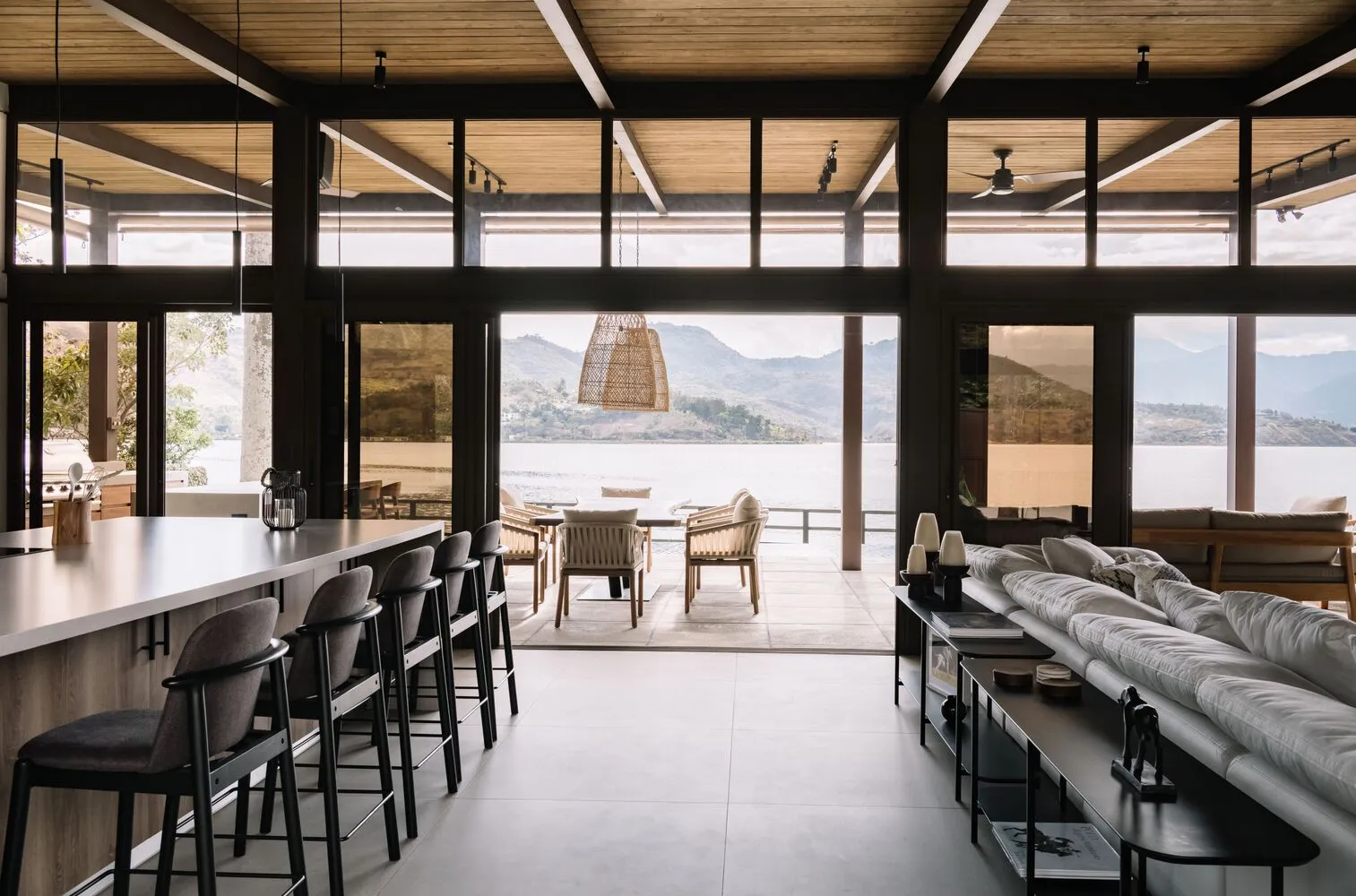 Modern living room with glass walls overlooking a beautiful lake and mountains, featuring sleek furniture and large windows f
