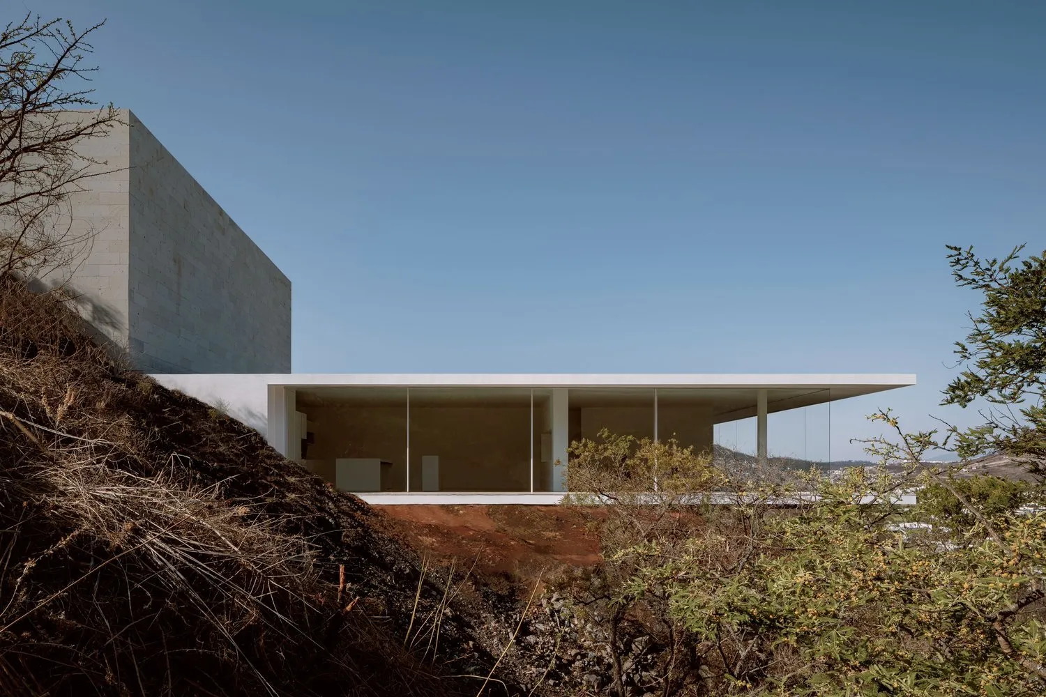 A modern residential living room with concrete walls and large glass windows.
