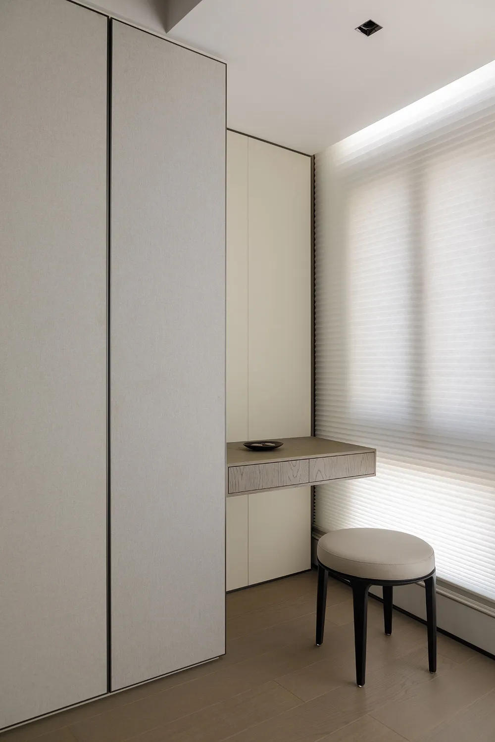 A minimalist study space featuring neutral-colored furniture and a window with sheer blinds.