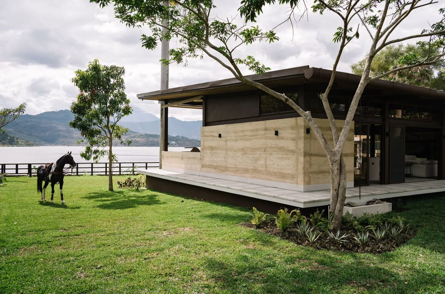 A modern house with a concrete exterior and glass windows overlooking a landscape.