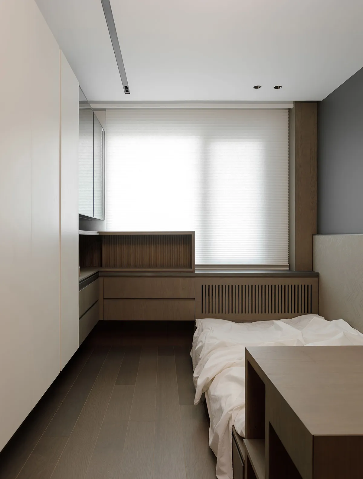 A modern minimalist bedroom featuring wooden cabinets and a bed.