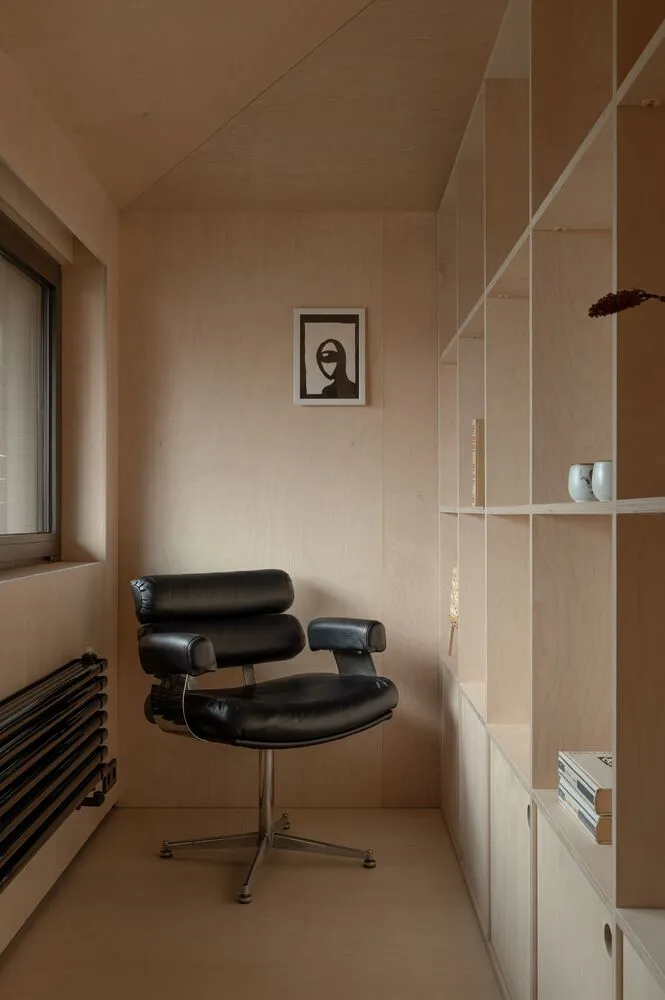 A minimalist home office with a black chair and wooden shelves.