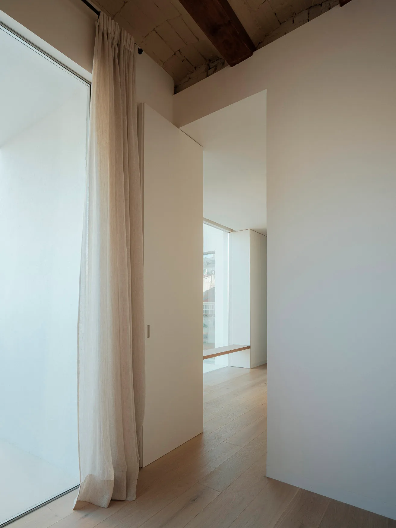 Interior space featuring minimalist design with wooden flooring, glass window, and white walls.