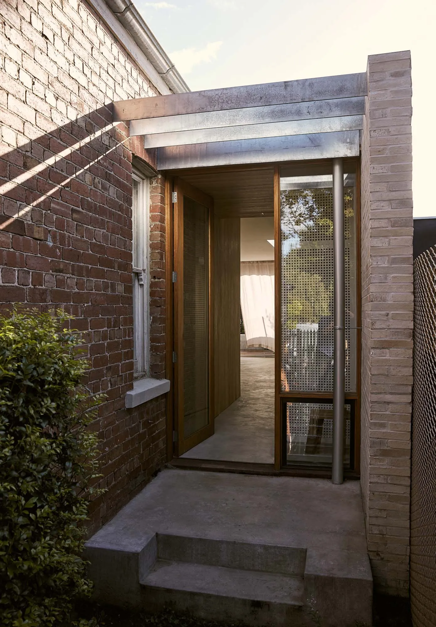 An entrance designed with brick walls, concrete steps, and aluminum framework.