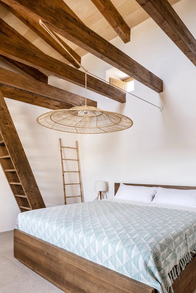 Minimalist bedroom featuring wood beams, wicker chandelier, and fabric bedding.