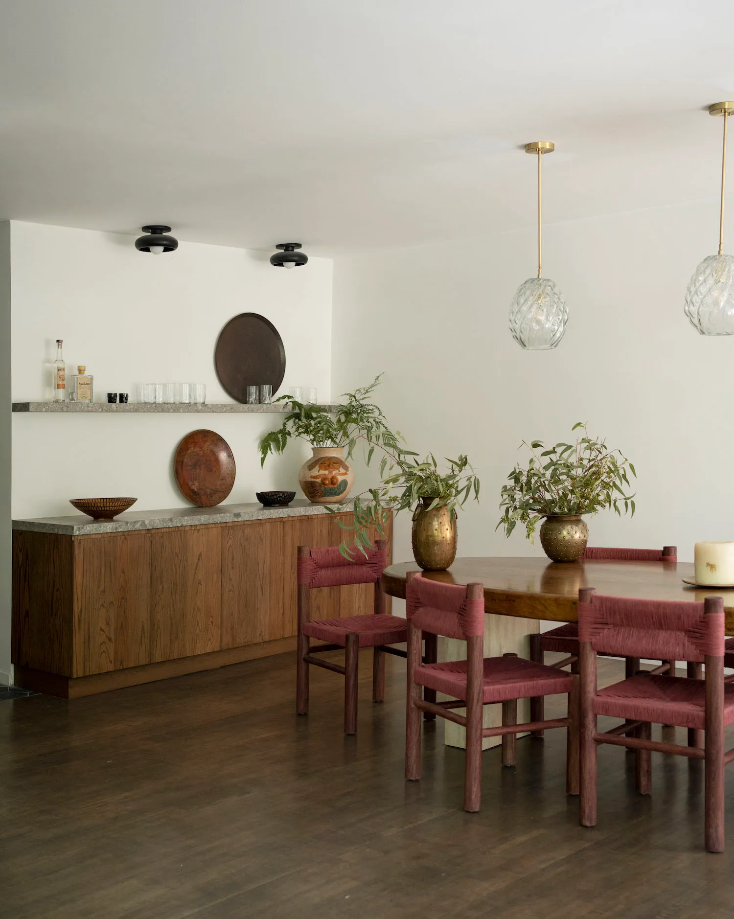 A modern dining room featuring wooden furniture, including a round wooden table, red woven chairs, and a shelf with decorativ