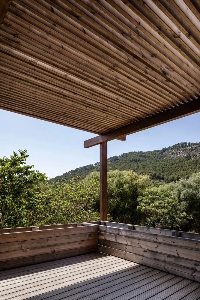 Modern outdoor deck featuring a wooden lattice overhead, surrounded by lush greenery and hills in the background.