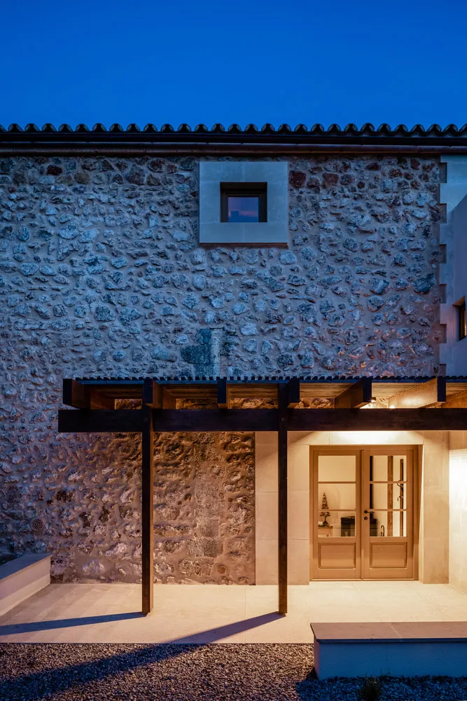 A stone building entrance with a wooden pergola at dusk.