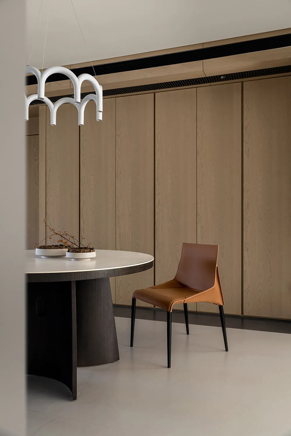 Modern dining room with wooden furniture and minimalist decor, featuring a round table, leather chair, and geometric light fi