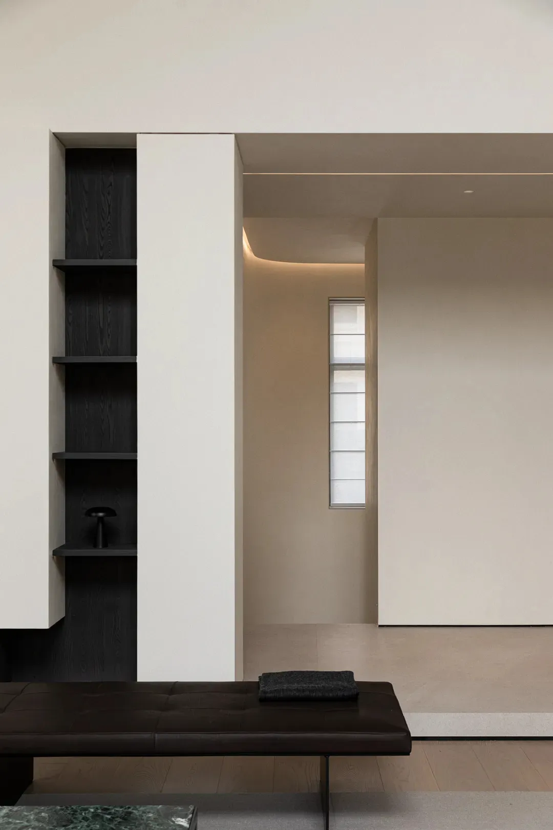 A minimalist interior showcasing a white concrete wall and floor, with a black shelf and a black bench.