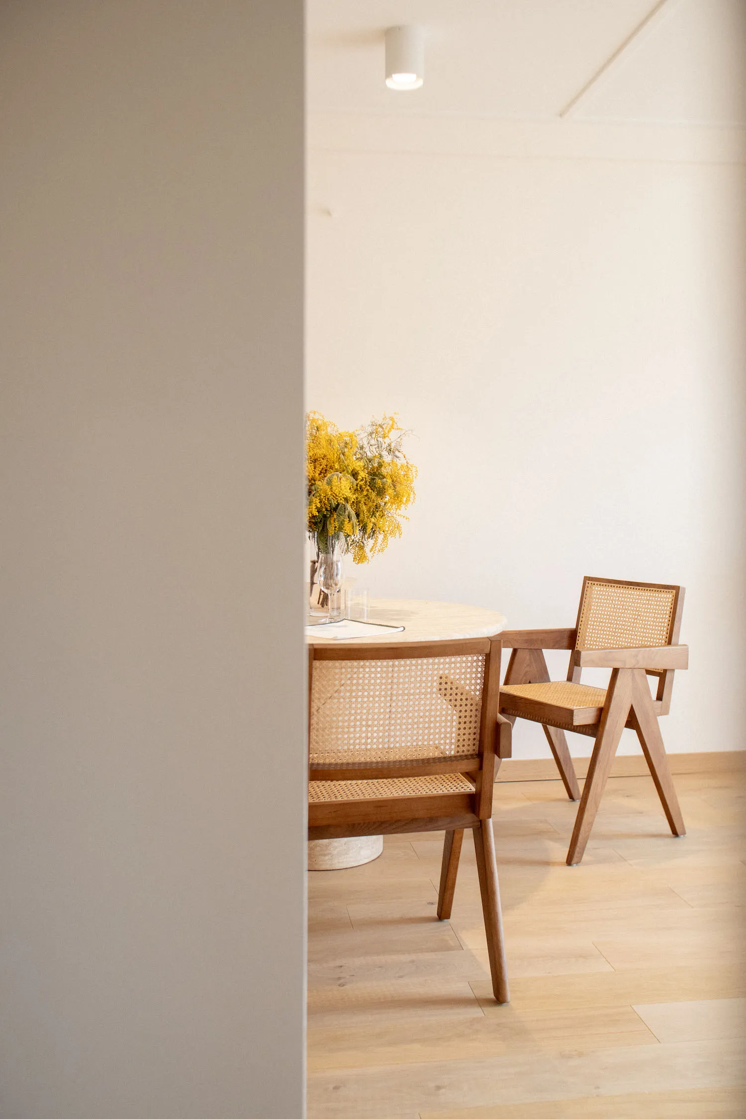 Modern dining room with wooden furniture and a vase of yellow flowers.