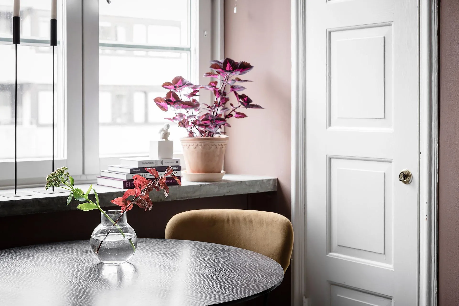 A modern residential interior with a wooden table, a vase with flowers, a potted plant, and a beige chair.