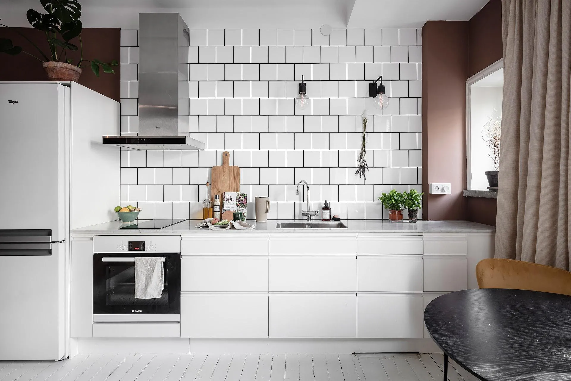 A minimalist modern white kitchen with white subway tiles and stainless steel appliances.