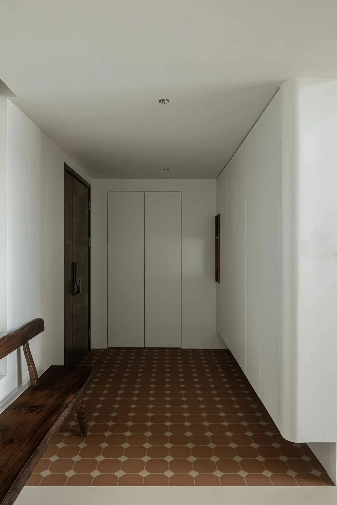 A minimalist entryway featuring a tiled floor and wooden bench against white walls.