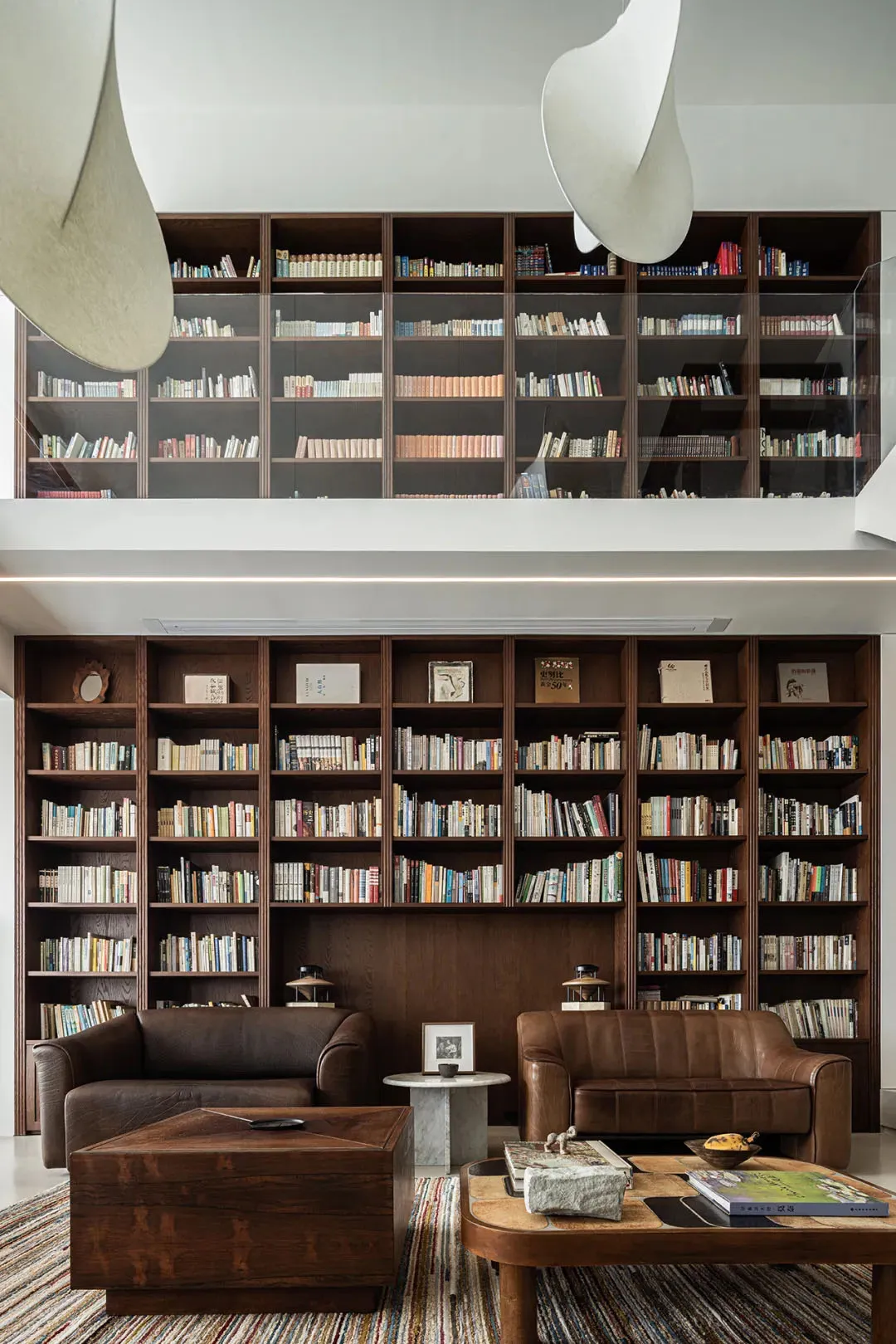 A modern reading room featuring wooden shelves filled with books, two brown leather sofas, and a wooden coffee table with var