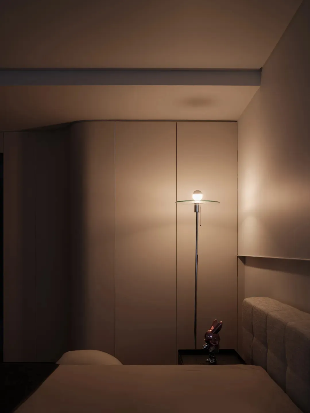 Minimalist bedroom featuring a glass night light floor lamp and a nightstand with a toy rabbit.