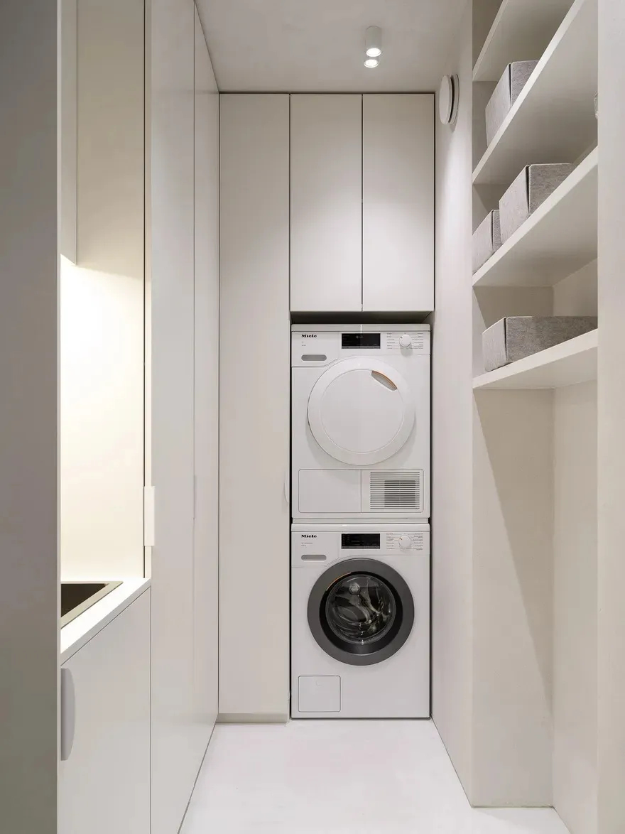 A minimalist laundry room with a white cabinet, washing machine, dryer, and organized shelves.